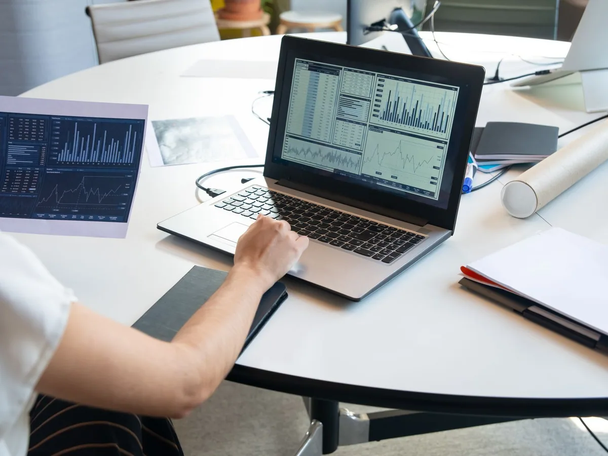 Person comparing a printed report with charts on a laptop
