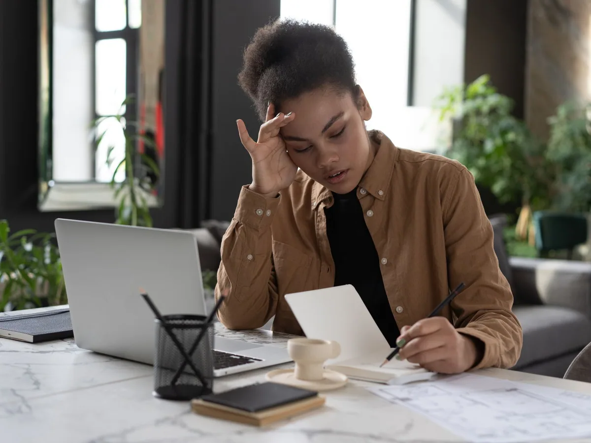 Woman drafting notes beside her laptop in a bright workspace