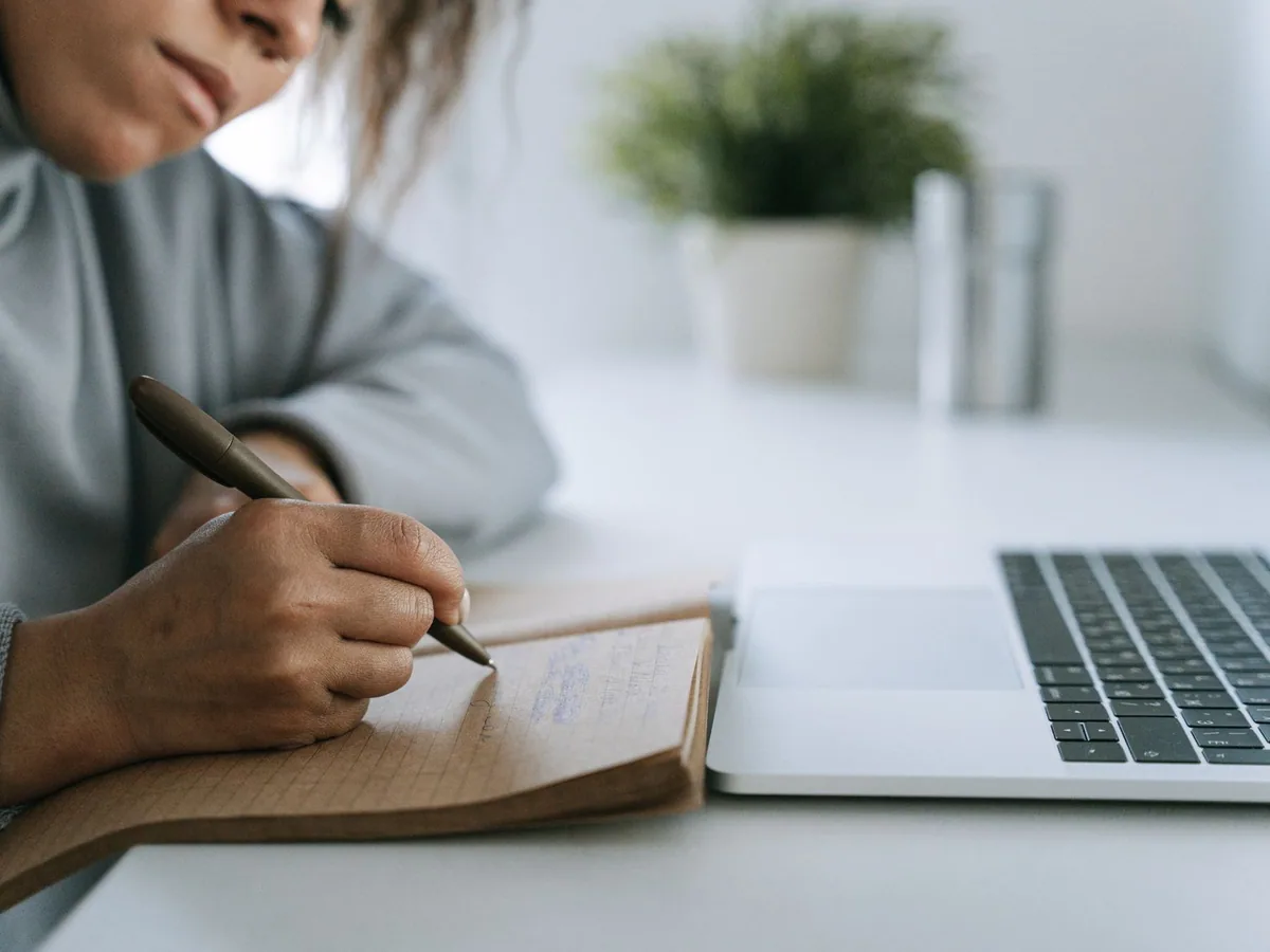 Close-up of a person taking notes beside a laptop